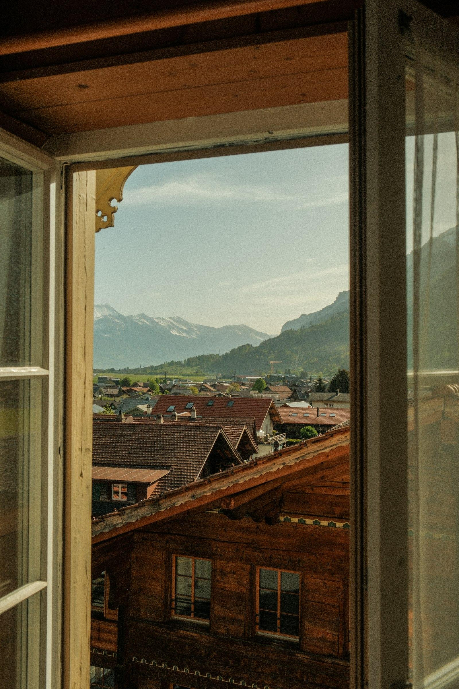 Open wood-frame window looking out across a Sierra foothills village to the mountains beyond — illustrating gas-filled insulated glass units in foothill homes